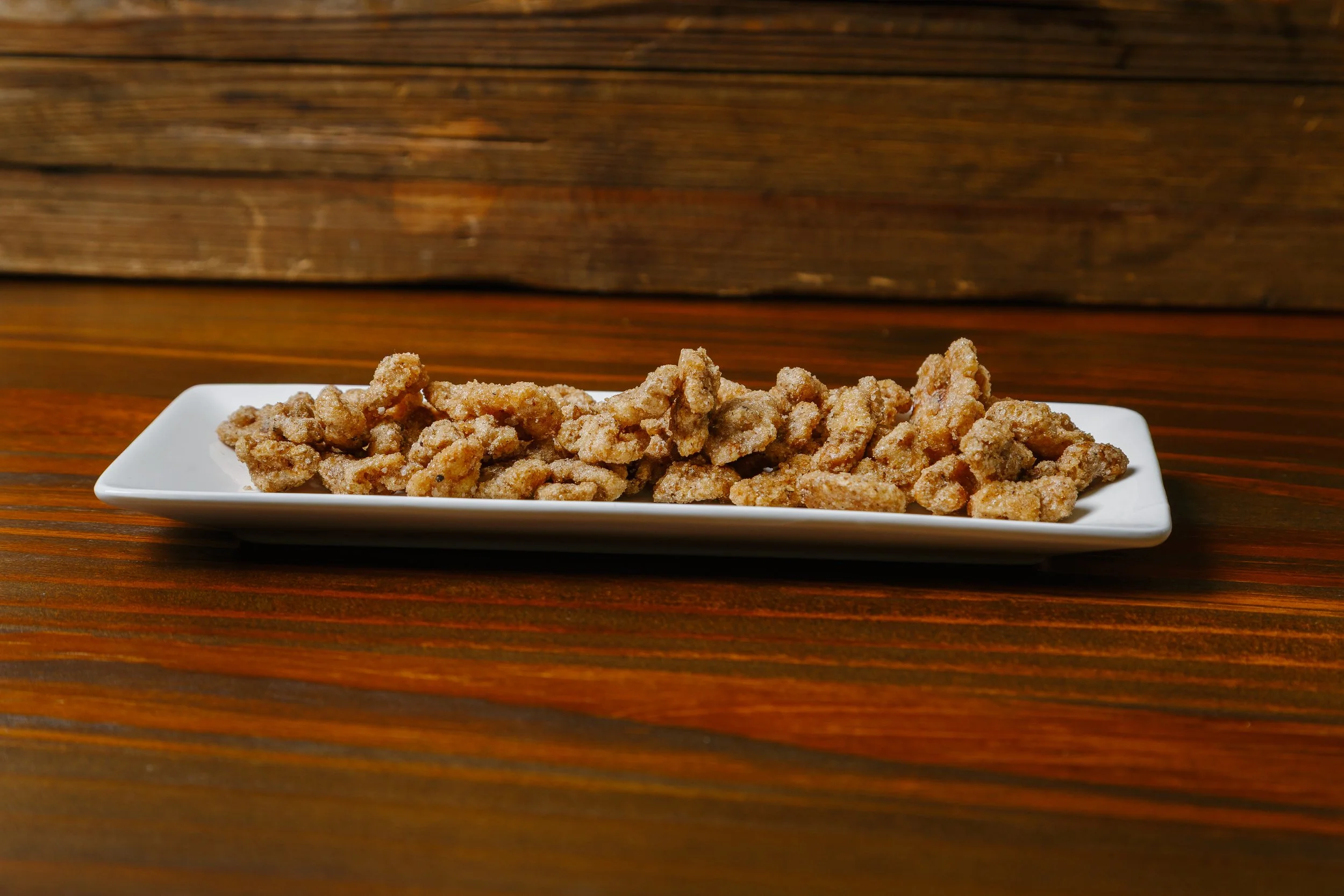 Fried chicken pieces on a white rectangular plate placed on a wooden surface with a wooden background.
