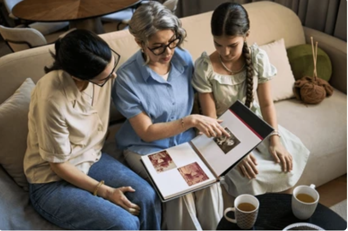 An older woman sitting with two younger people looking at a photo album