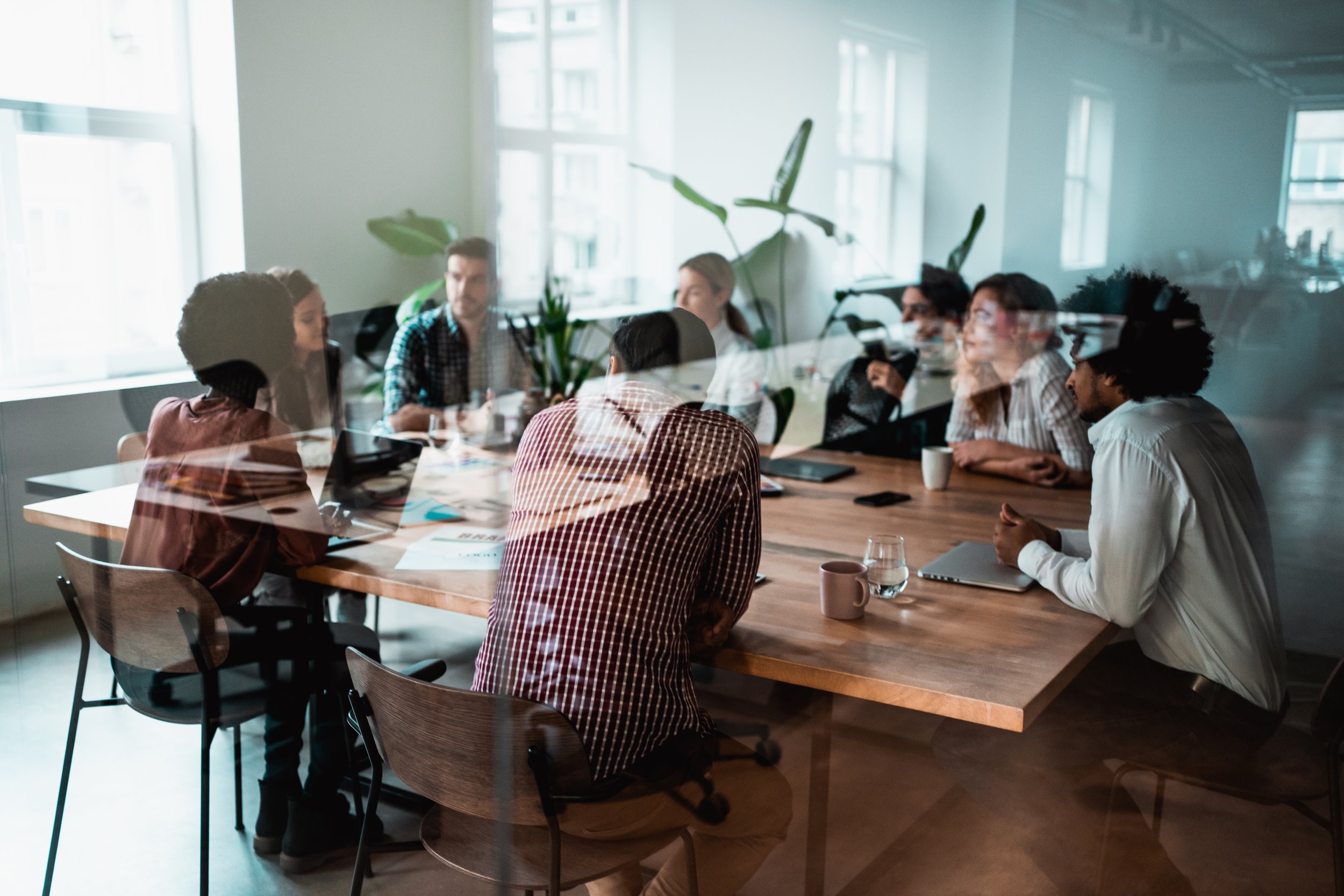 Shot through glass, a group of people working together sat around a squared wooden desk