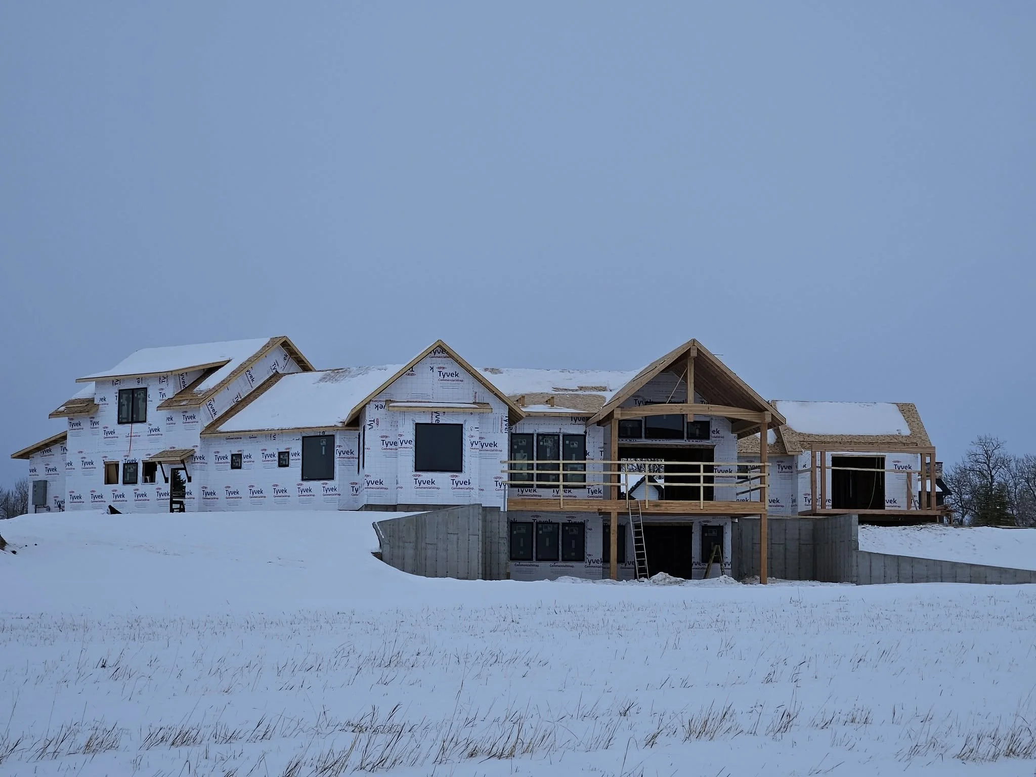 A house under construction in a snowy landscape with a clear sky.
