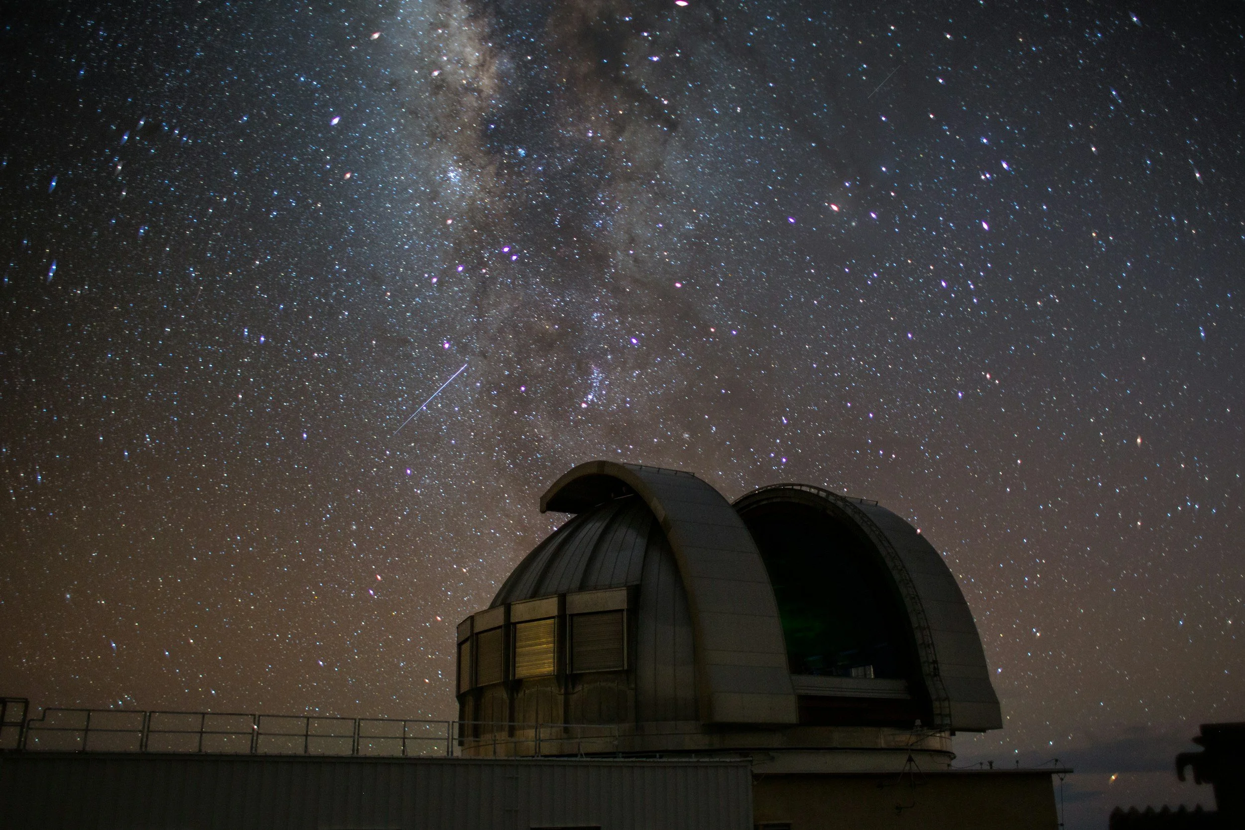 An observatory building with a domed roof set against a night sky filled with stars and the Milky Way galaxy visible overhead.