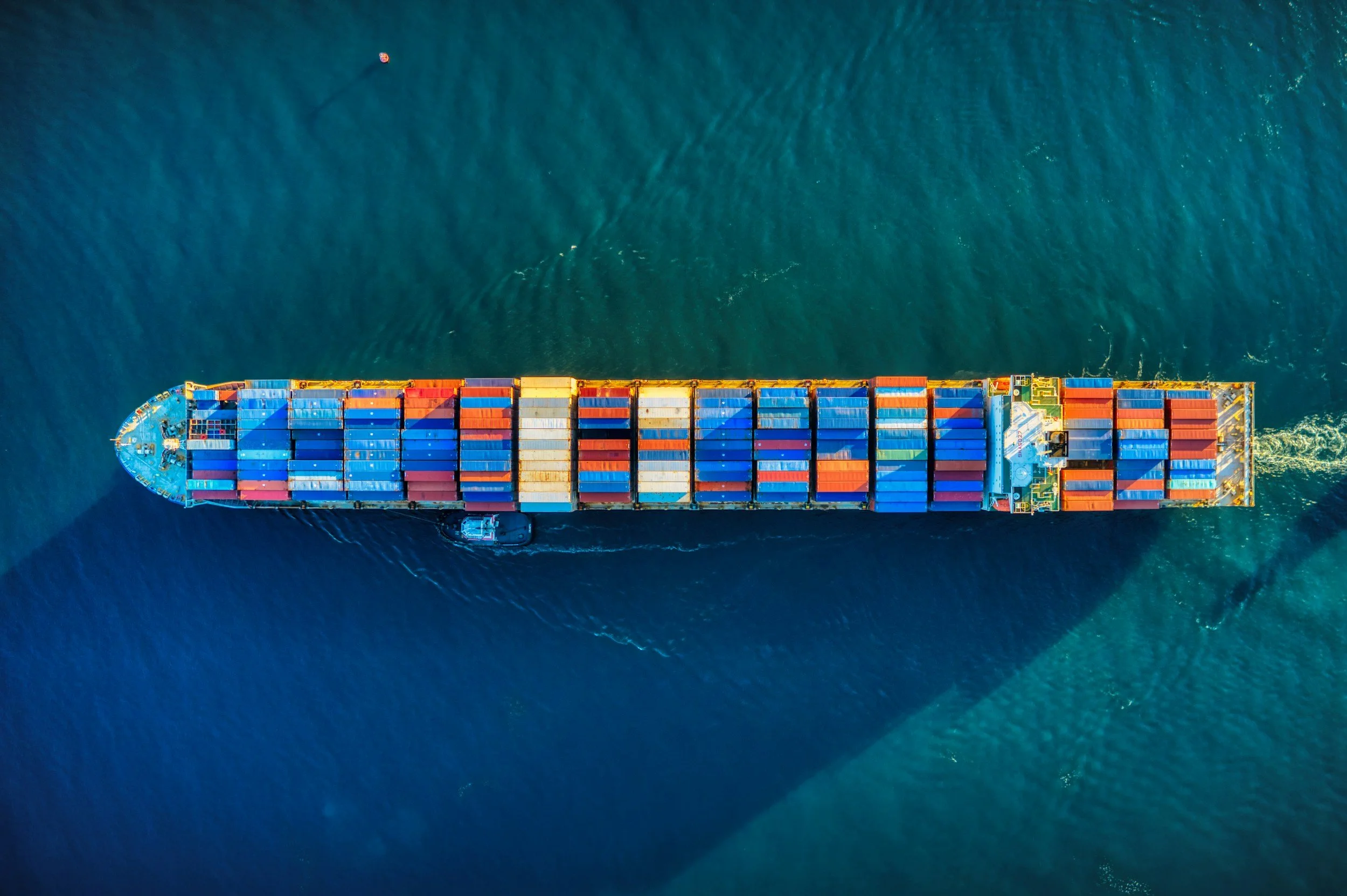 Aerial view of a large cargo ship carrying multicolored shipping containers navigating through deep blue water.