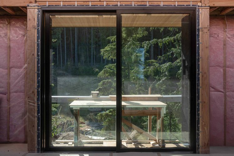 Black sliding door in an unfinished wall with pink insulation, a work table on the deck beyond