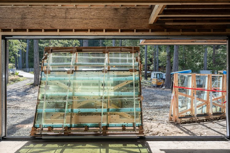 Crated glass units standing inside an unfinished opening, trees and a loader beyond