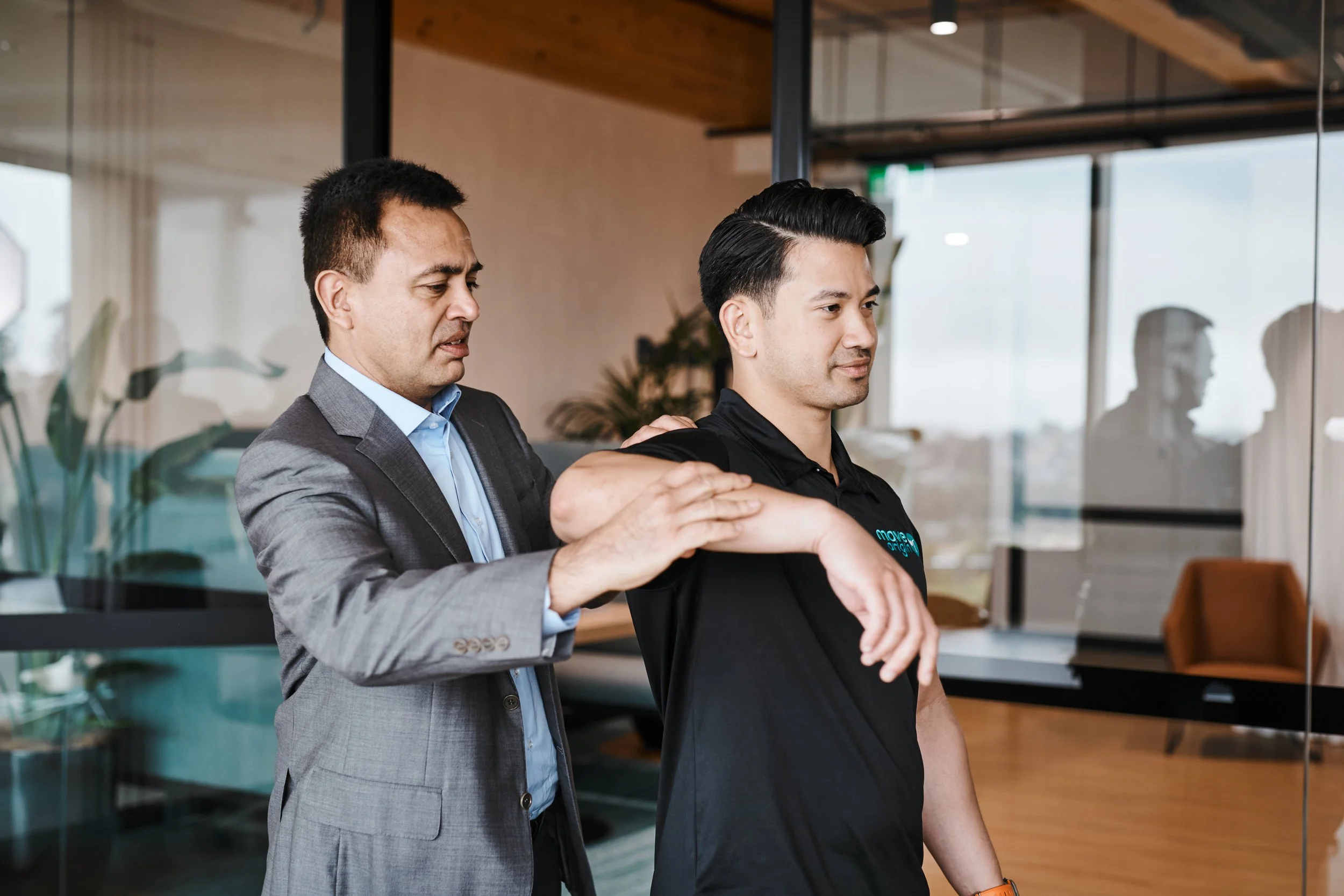 A chiropractor performing a shoulder adjustment on a young man in a modern office space.