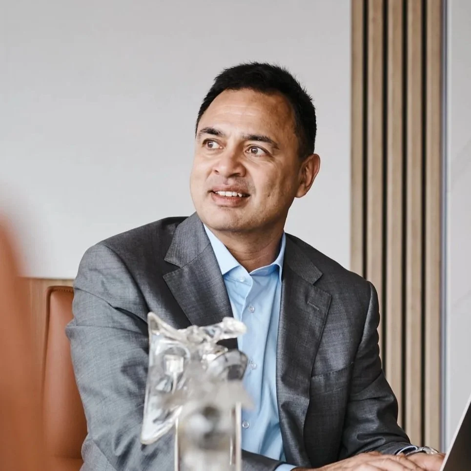 Businessman in a gray suit sitting at a table in a meeting room.