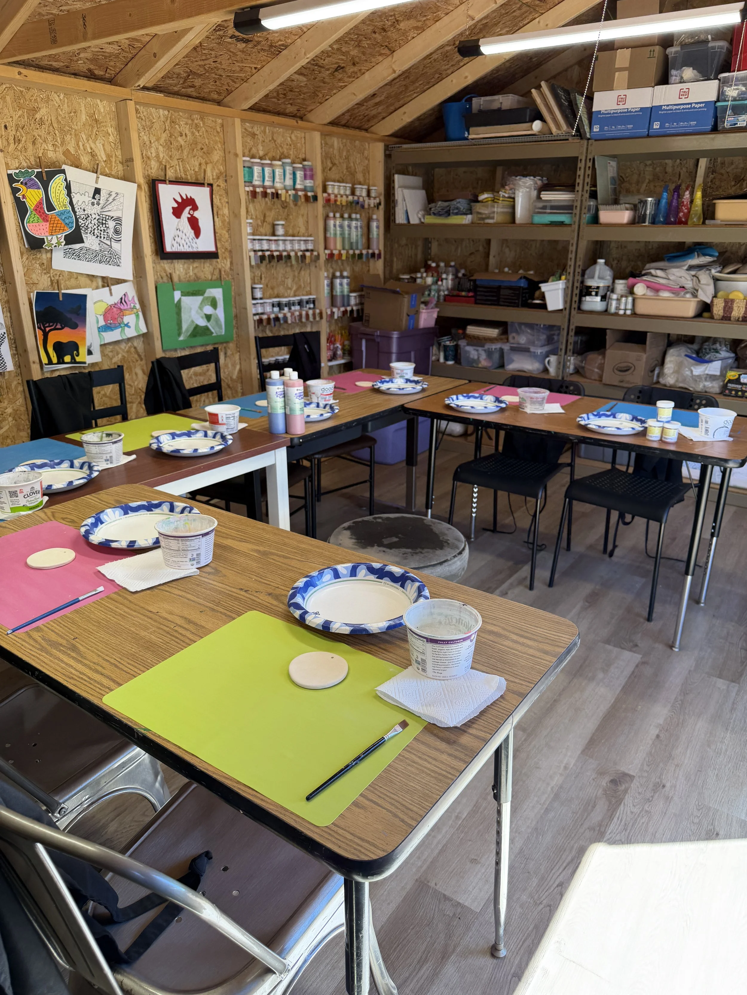 An art workspace with paintbrushes, a cup of black coffee, watercolor paintings on paper, and a small palette with black and gray paint.