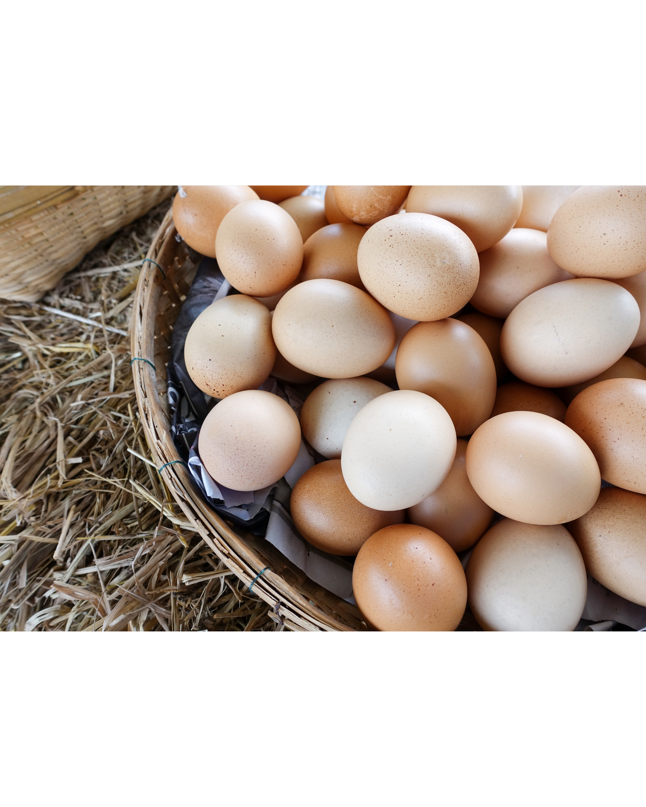 A basket of fresh brown eggs on a bed of straw.