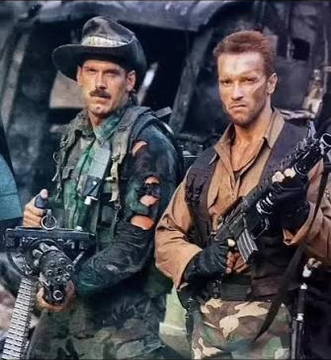 Blain and Dutch standing together in Predator, both heavily armed