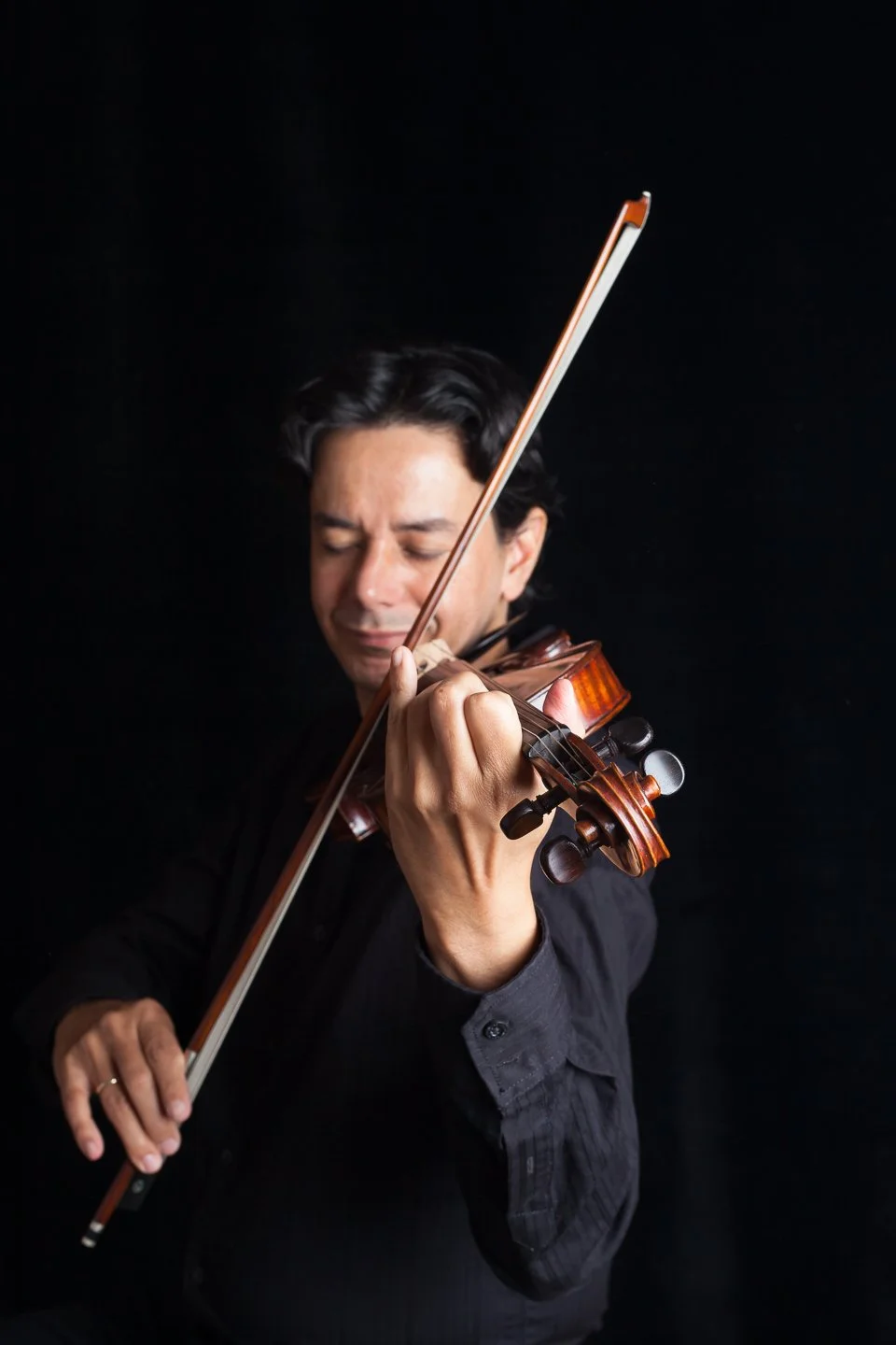 A man playing the violin with his eyes closed against a black background.