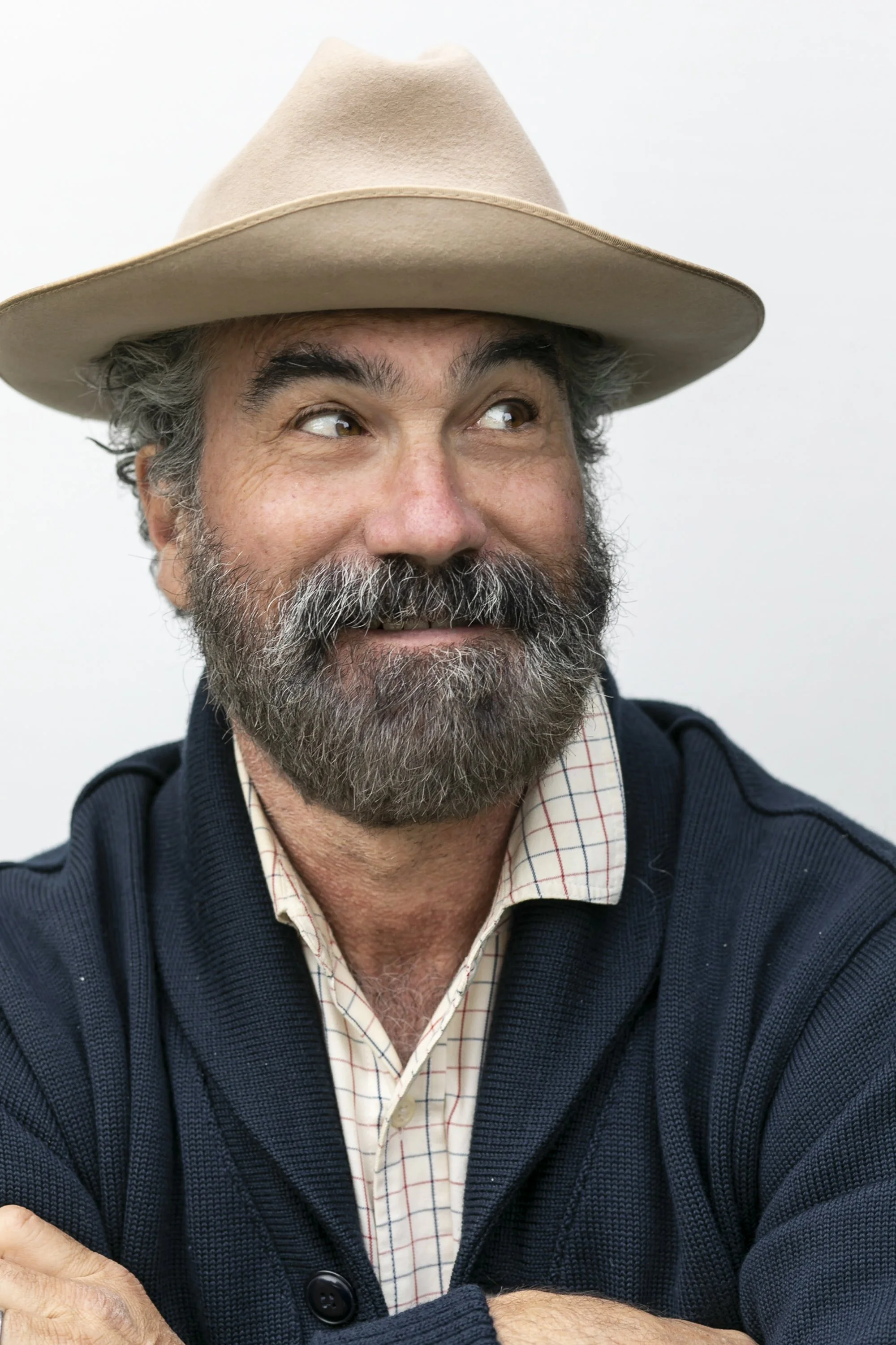 A middle-aged man with a beard and mustache wearing a beige hat and a navy blue sweater, smiling and looking to the side.