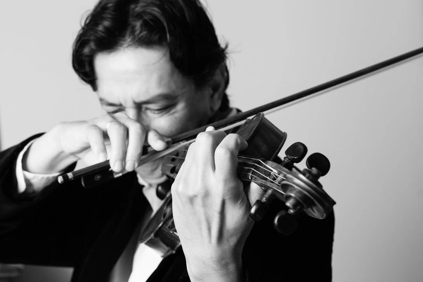 Man playing a violin, seen in black and white, with his eyes closed and focused on the instrument.