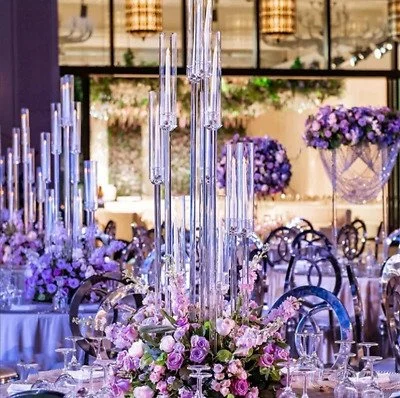 Elegant banquet table decorated with tall glass candle holders and a floral centerpiece of purple and pink flowers in a grand dining hall.