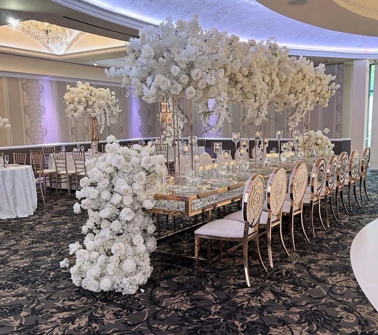Elegant banquet table decorated with white floral arrangements in tall vases and candles, set in a luxurious banquet hall.