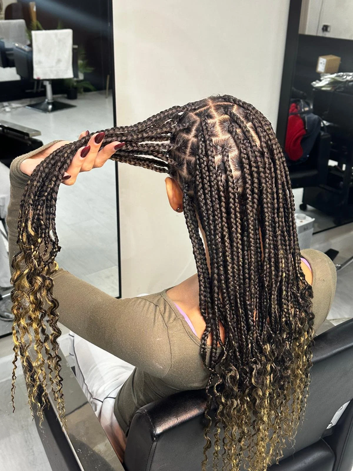 A woman in a salon, having her hair styled into neat, medium-sized box braids with the ends curled.