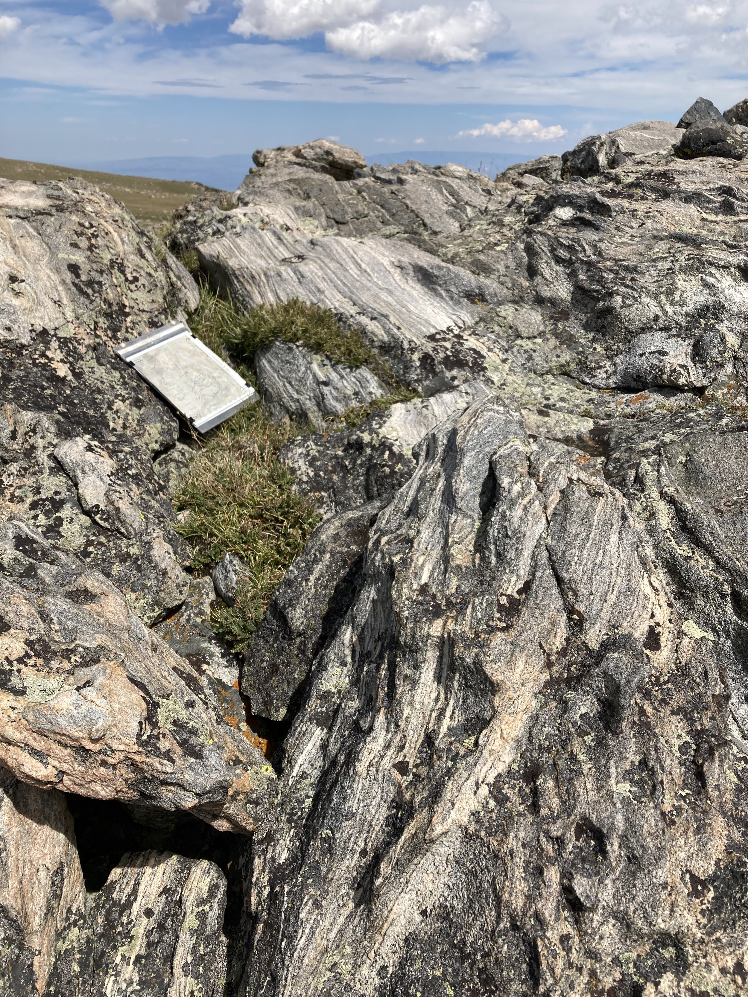 Large rocks and boulders in a mountainous landscape with a cloudy sky in the background. A small metal notebook is resting among the rocks.