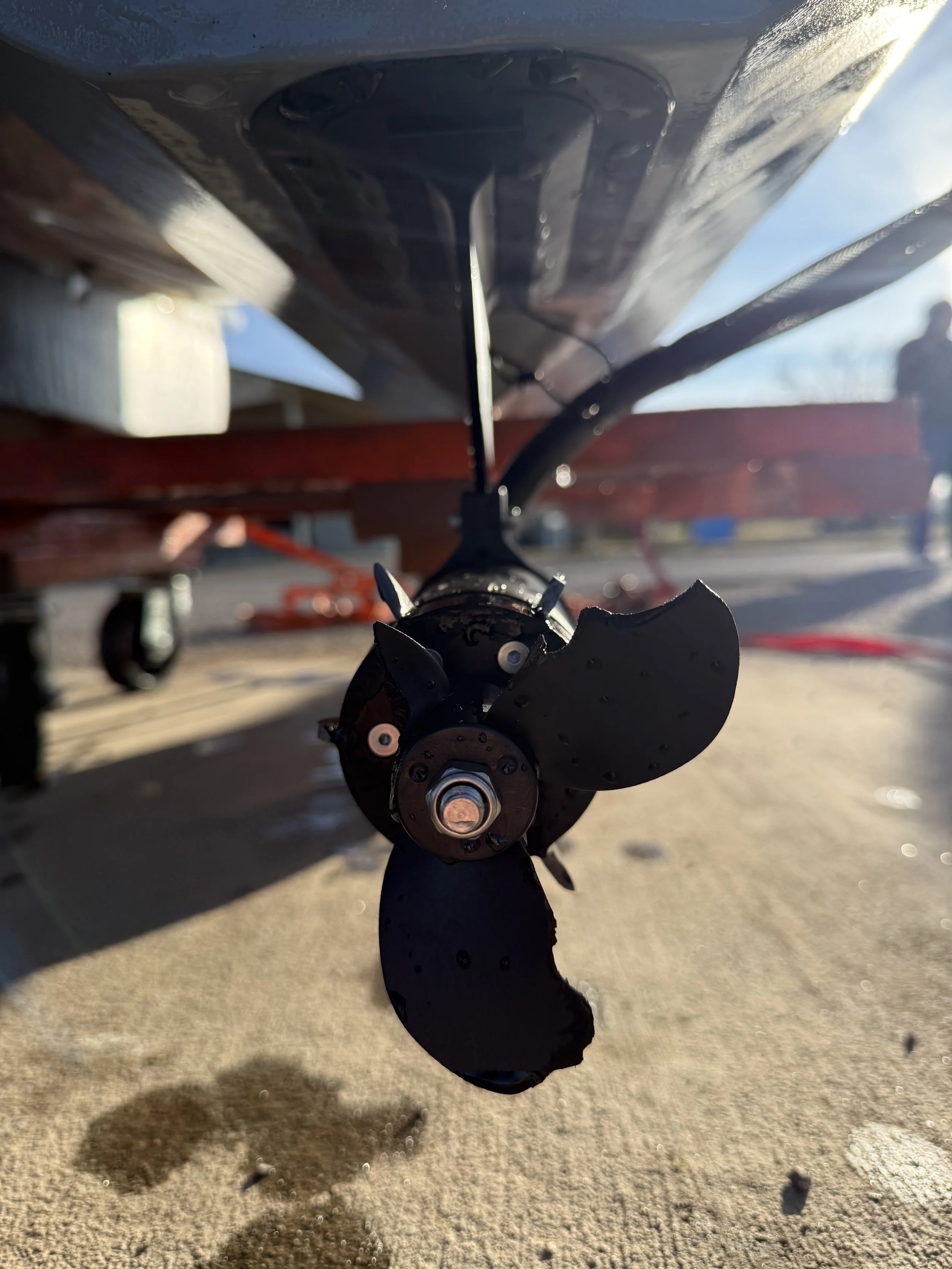 Boat propeller with three blades, mounted under the hull of a boat, on a concrete surface with shadows.