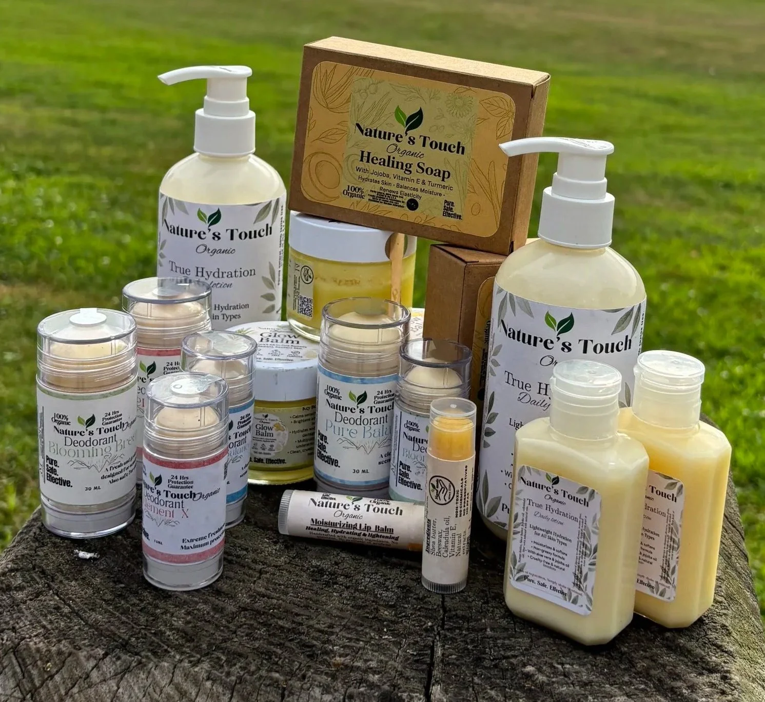 A collection of Nature's Touch organic skincare products, including hand soap, deodorants, moisturizing balm, and lip balm, arranged on a tree stump outdoors.