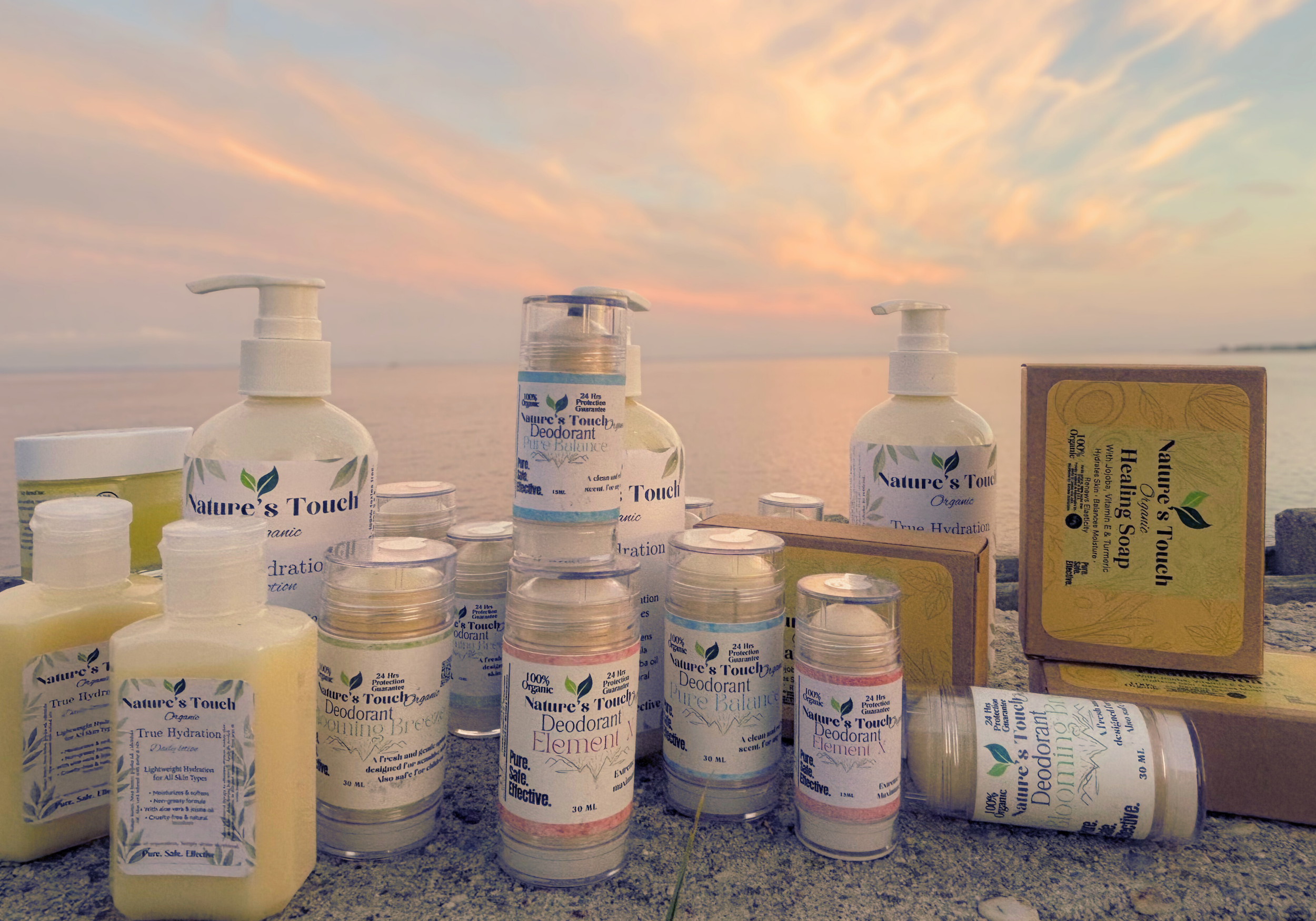 Various bottles and boxes of Nature's Touch organic deodorant and healing soap set on a sandy beach with a sunset sky in the background.