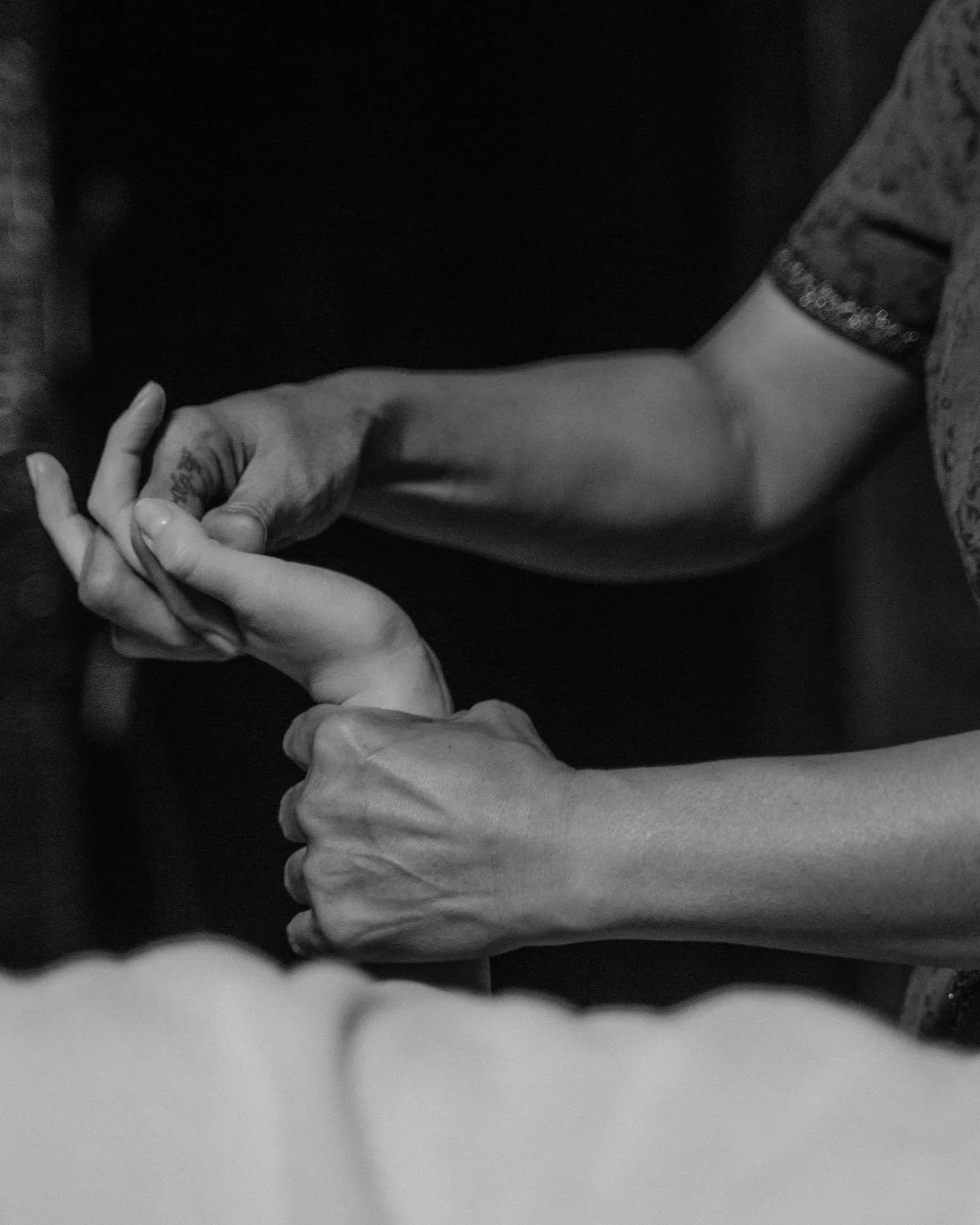 Two people with intertwined hands, one person's hand resting on top of the other's, in black and white.