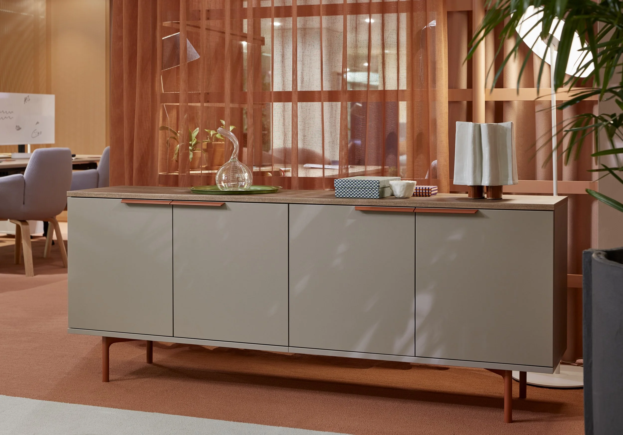 Modern living room with beige sideboard, decorative glass vase, boxes, and lamp on top, peach curtains, and beige carpet.