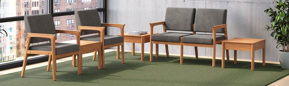 A waiting room with four wooden-framed chairs with gray cushions, a small wooden side table, and a potted plant on a green carpet near large windows showing a cityscape.