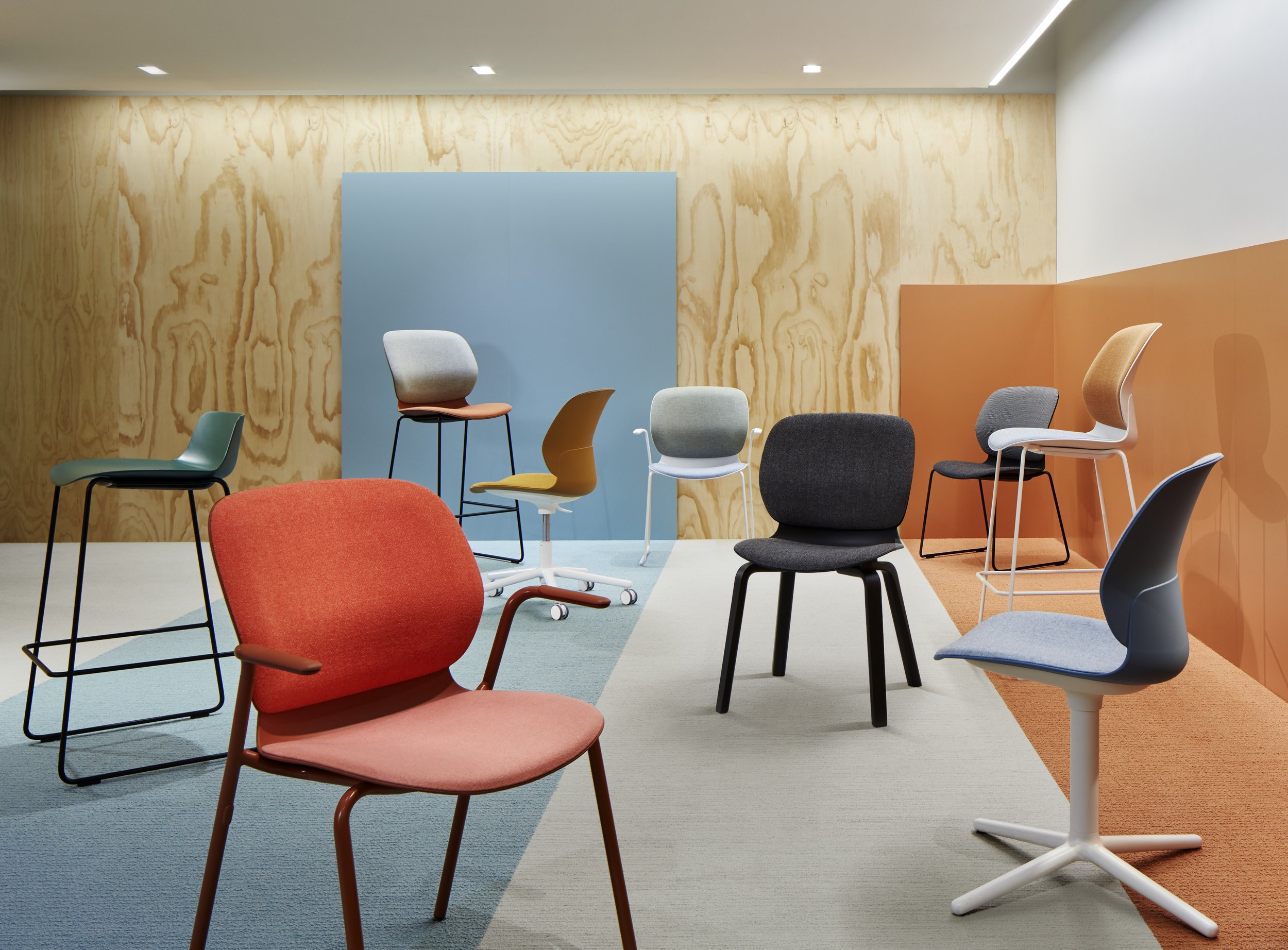 Colorful chairs arranged in a modern lounge or waiting area with wooden and painted wall backgrounds.