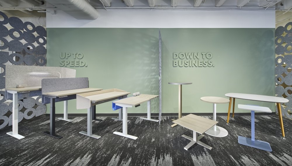 Display of adjustable desks and tables in a modern office space with motivational signs on the walls