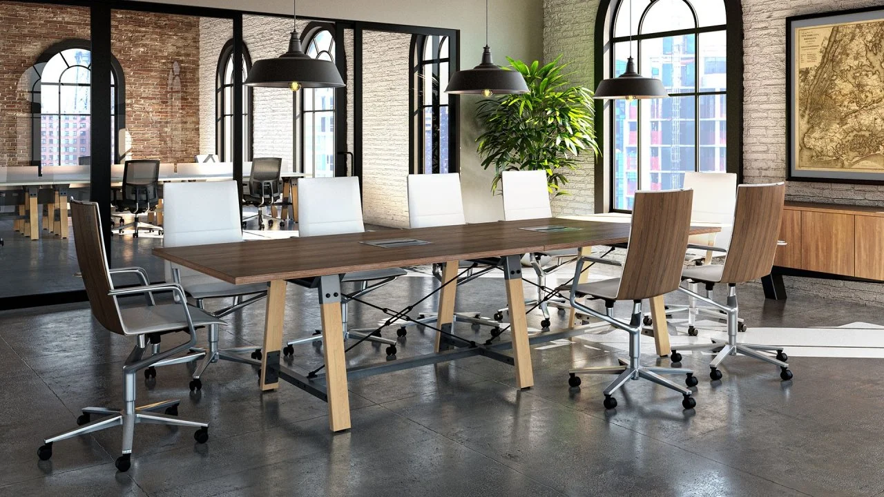 Modern meeting room with a long wooden table surrounded by white and wooden chairs, large windows, exposed brick walls, black pendant lights, and a potted plant.