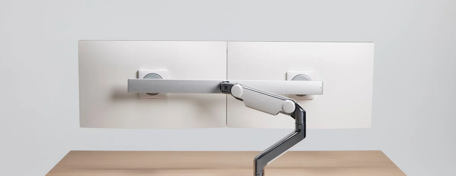 Desk with a monitor mounted using an adjustable arm, viewed from the back.