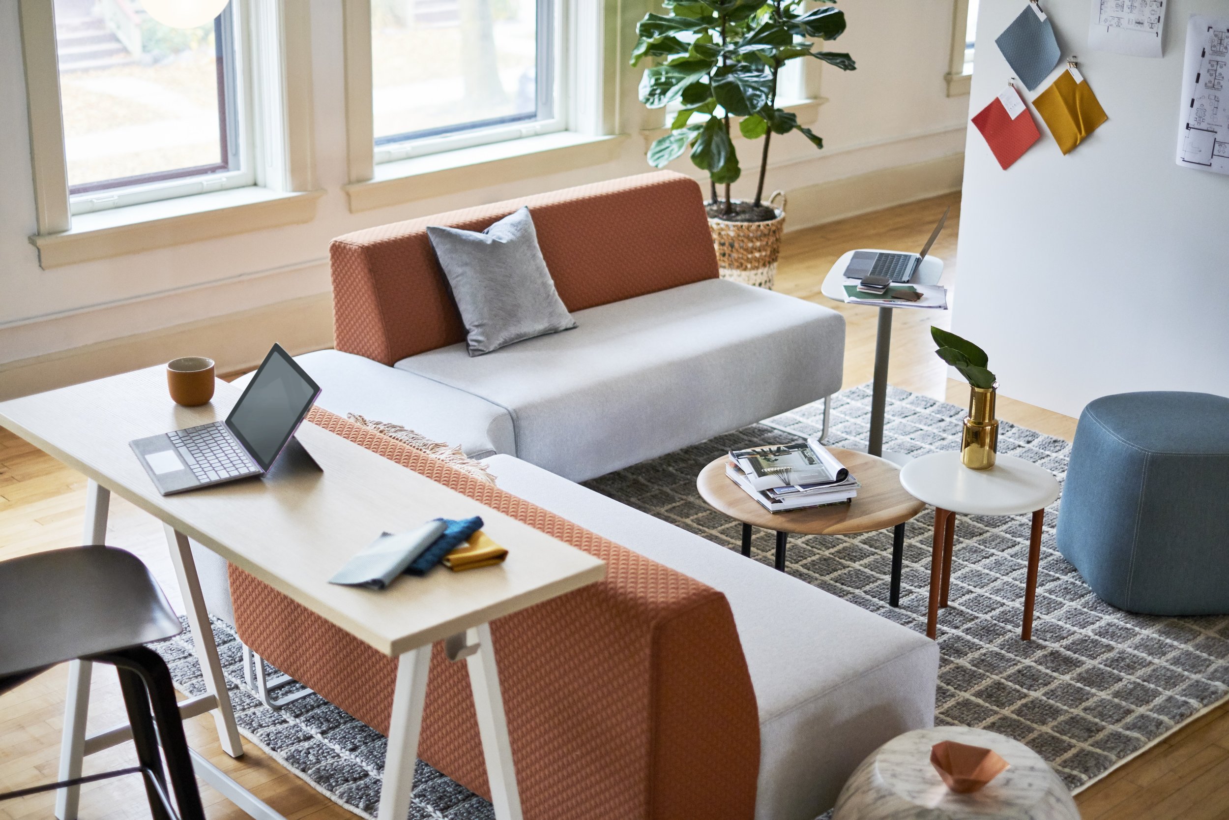 Modern living room with a large L-shaped sofa, coffee tables, a rug, potted plant, and large windows.