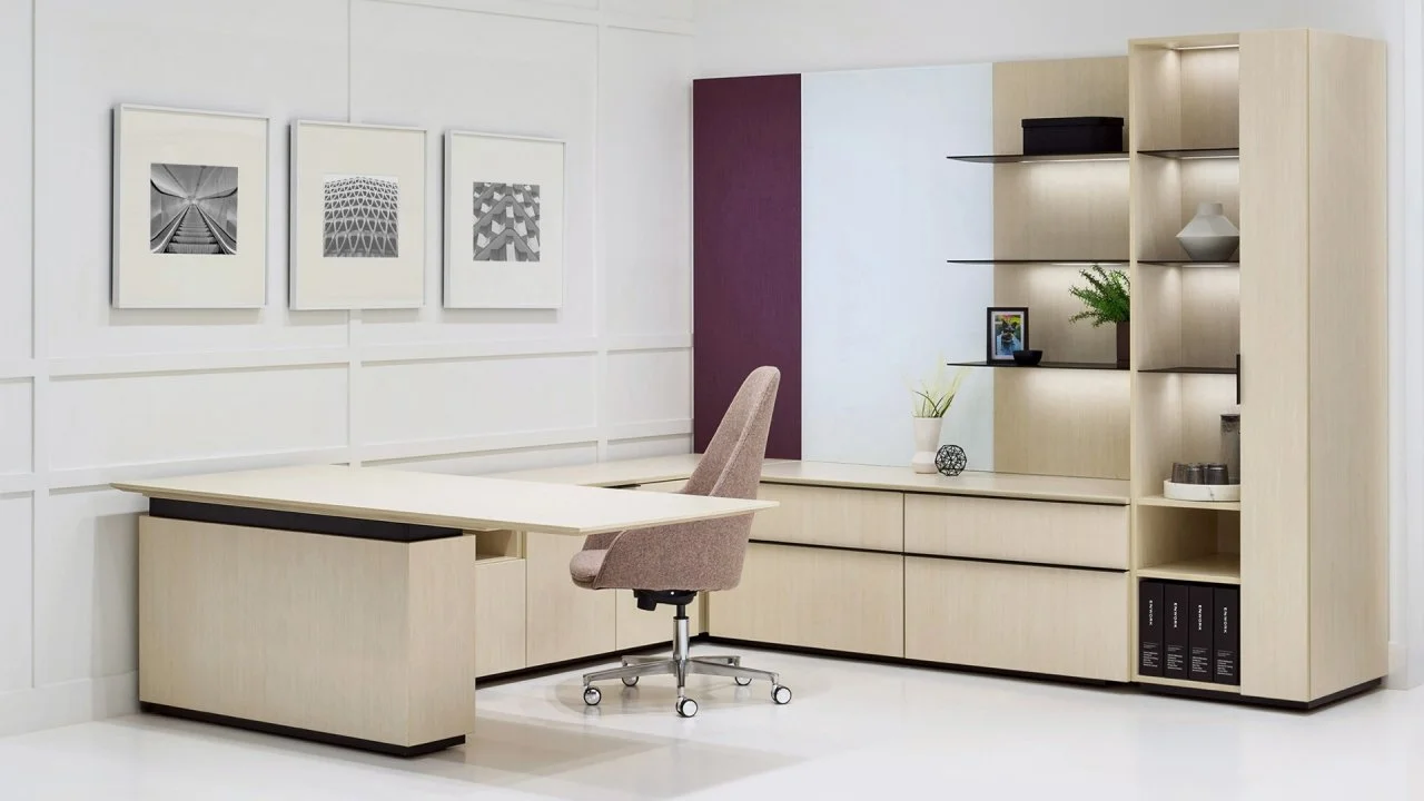 Modern office with beige desk, beige office chair, wall shelves, and black and white framed artwork.