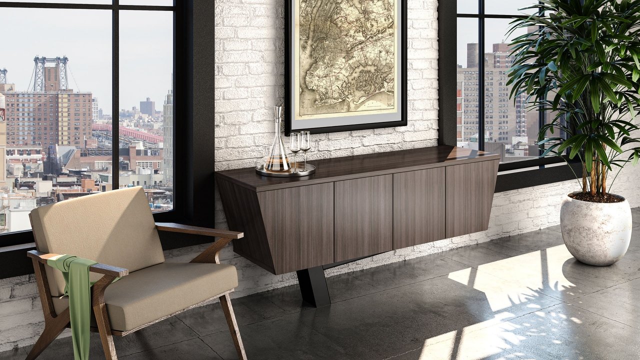 Modern interior with large windows, white brick wall, framed vintage map, wooden sideboard with decanter and glasses, armchair with green scarf, and large potted plant, overlooking city buildings.