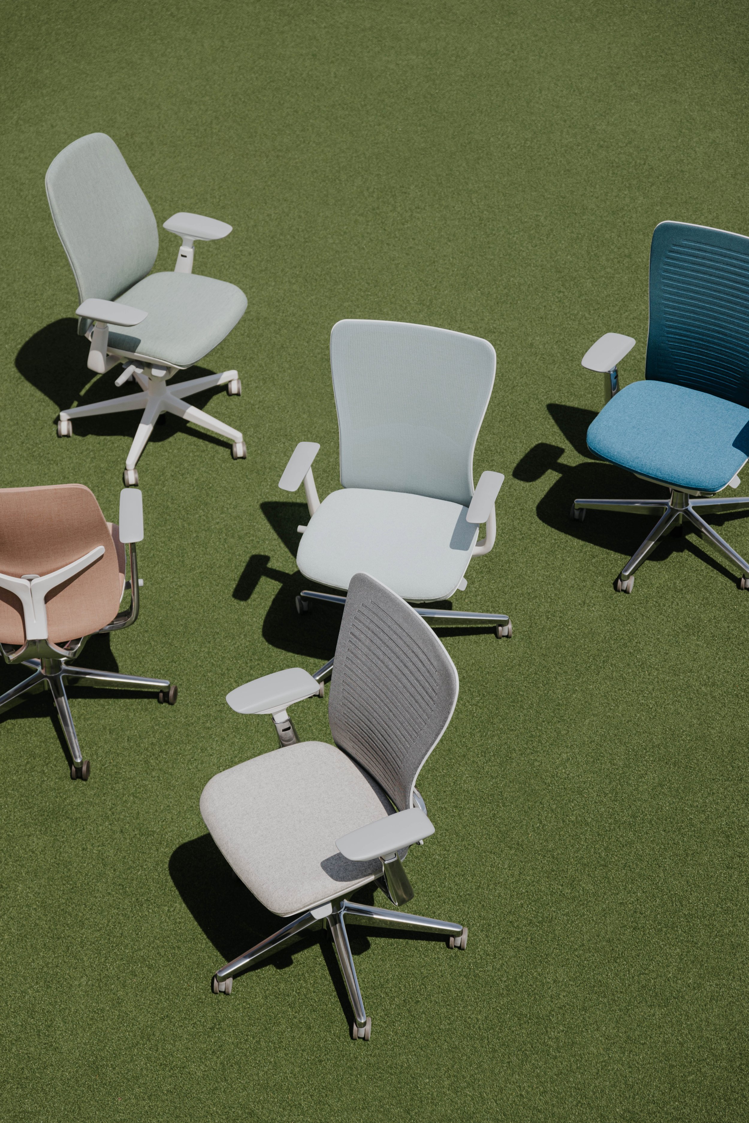 Several office chairs in different colors arranged on a green outdoor surface.
