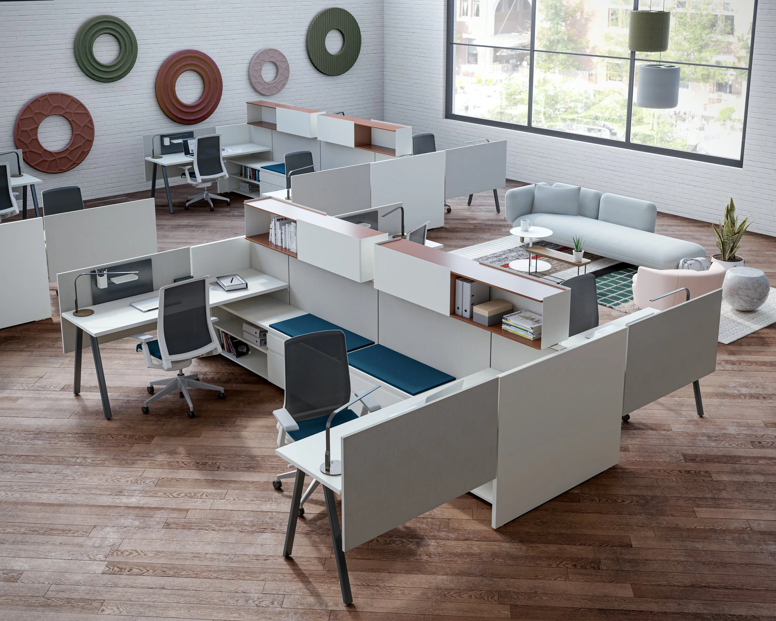 Open office space with desks, chairs, and a lounge area featuring a sofa and plants, illuminated by large window with view of trees outside.