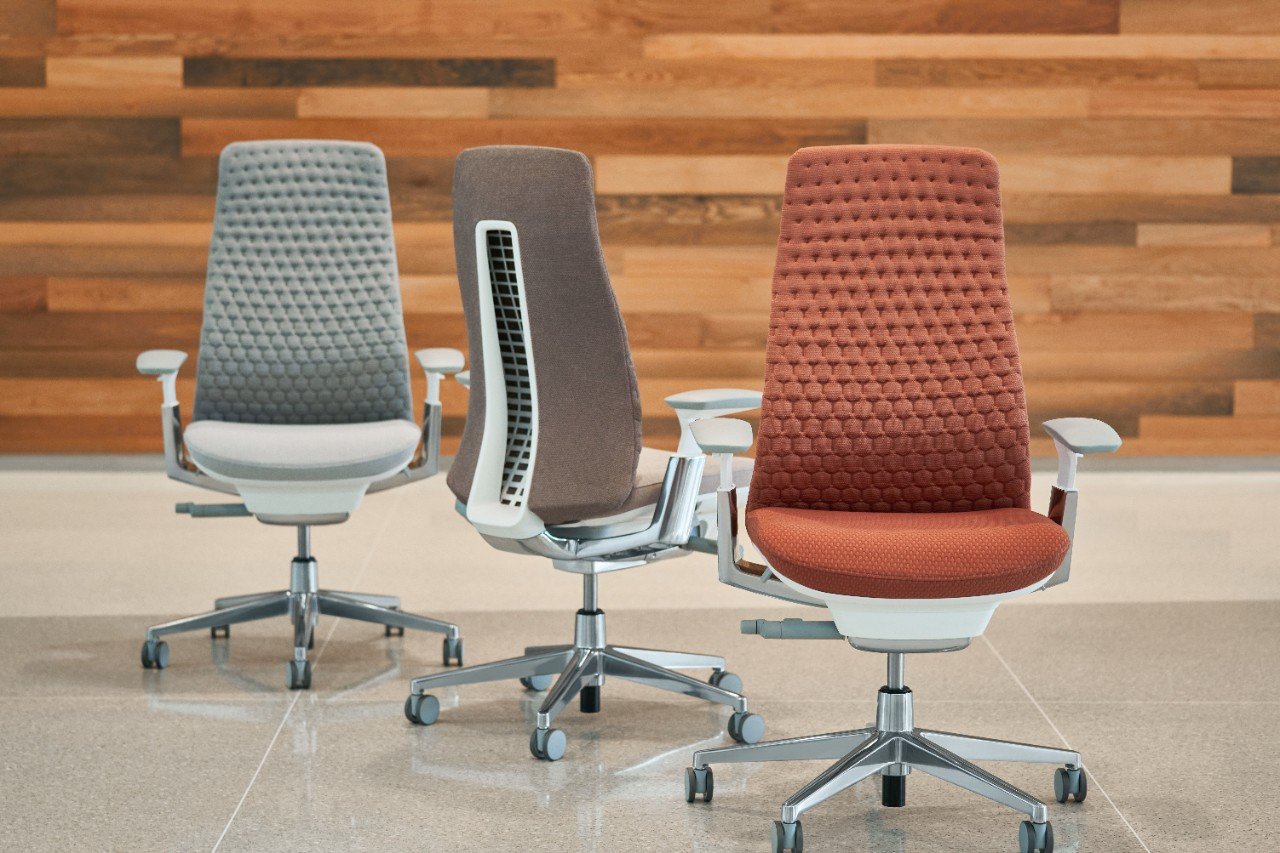 Three modern office chairs with different colored upholstery, positioned on a tiled floor in front of a wooden wall.