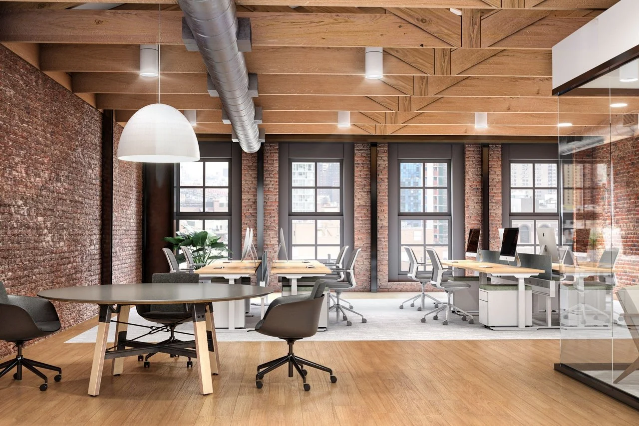 Modern office space with exposed brick walls, large windows, wooden ceiling, and multiple desks with computers.