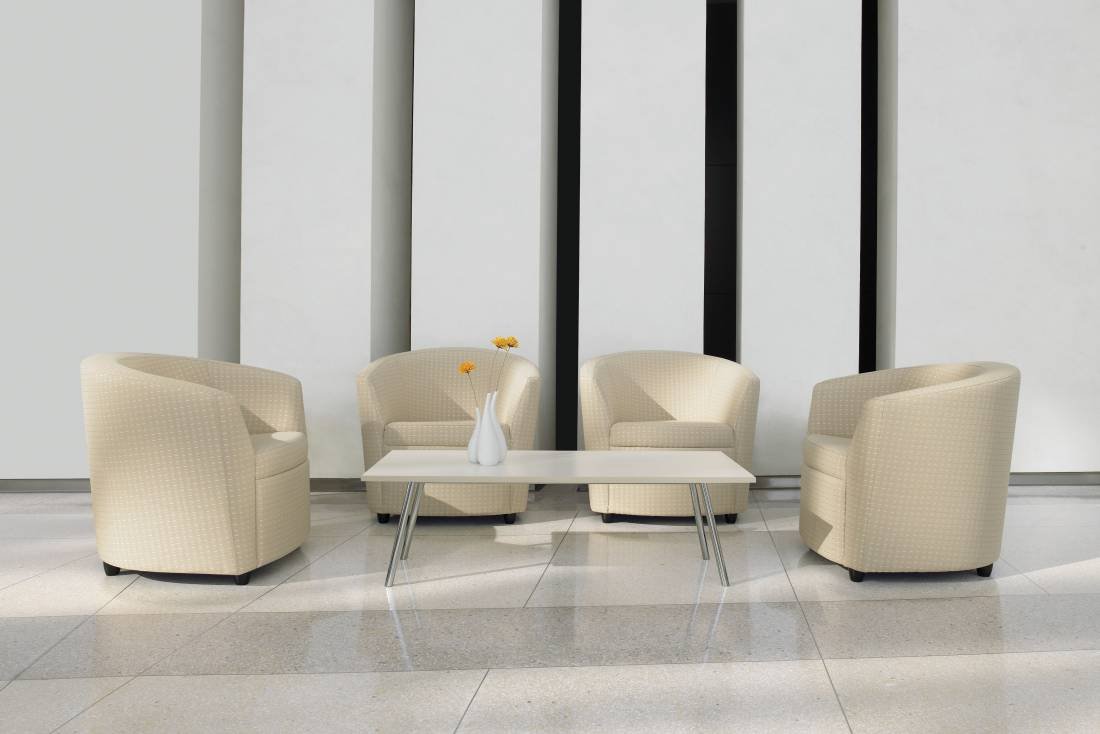 Four beige armchairs arranged around a white coffee table with a vase of flowers, set against a modern white wall with black vertical accents.