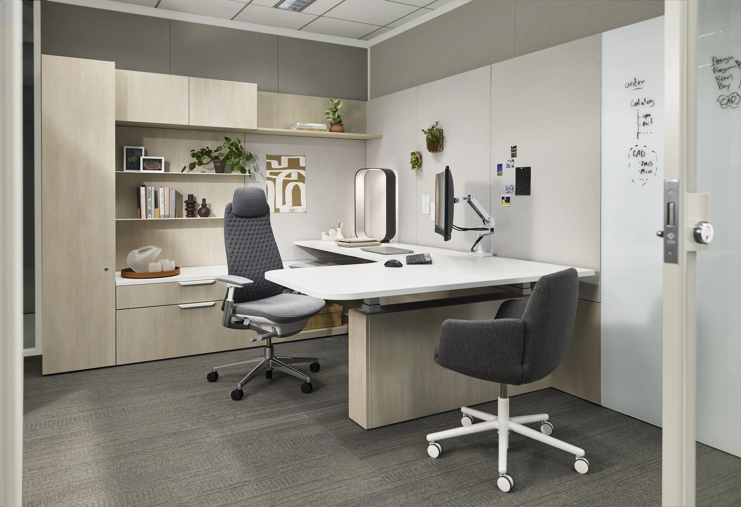 Modern office with a white desk, two gray office chairs, a beige storage cabinet, and wall-mounted shelves with plants and decorative items.