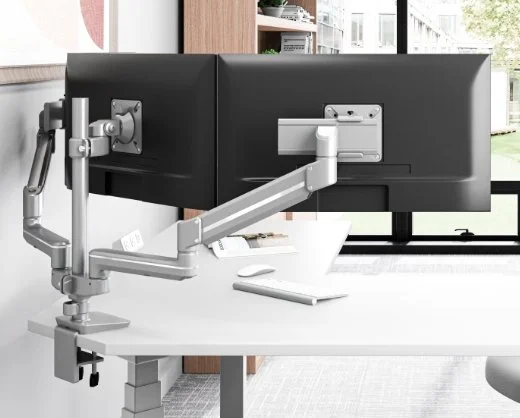 Adjustable monitor arm attached to a black computer monitor on a white desk in a modern office setting.