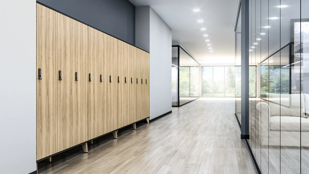 Modern corridor with wooden lockers on the left and glass-walled rooms on the right, with a bright view of trees outside at the end of the hallway.