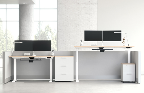 Two modern office desks with dual monitors, drawers, and minimal decor in a bright, minimal office space.