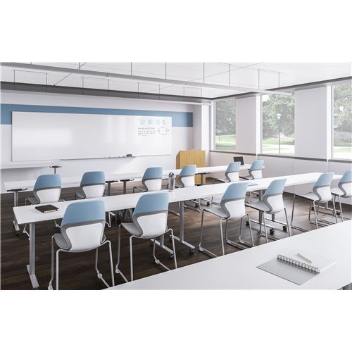 Empty modern classroom with white desks, blue and white chairs, large windows, and a whiteboard at the front.