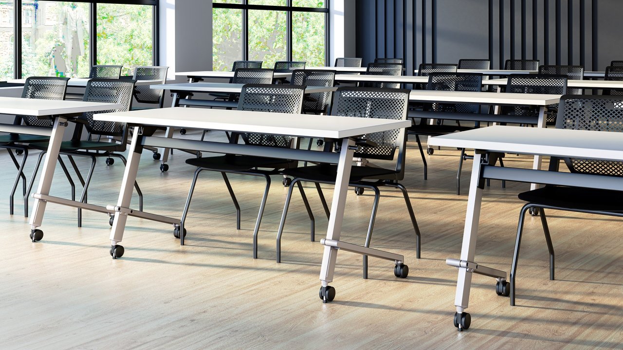 Empty conference room with white tables and black chairs, large windows with trees outside