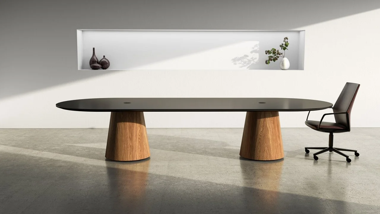 Modern office space with a long, oval black table with wooden base and a black ergonomic office chair. White wall with a recessed shelf holding three vases and a small potted plant.