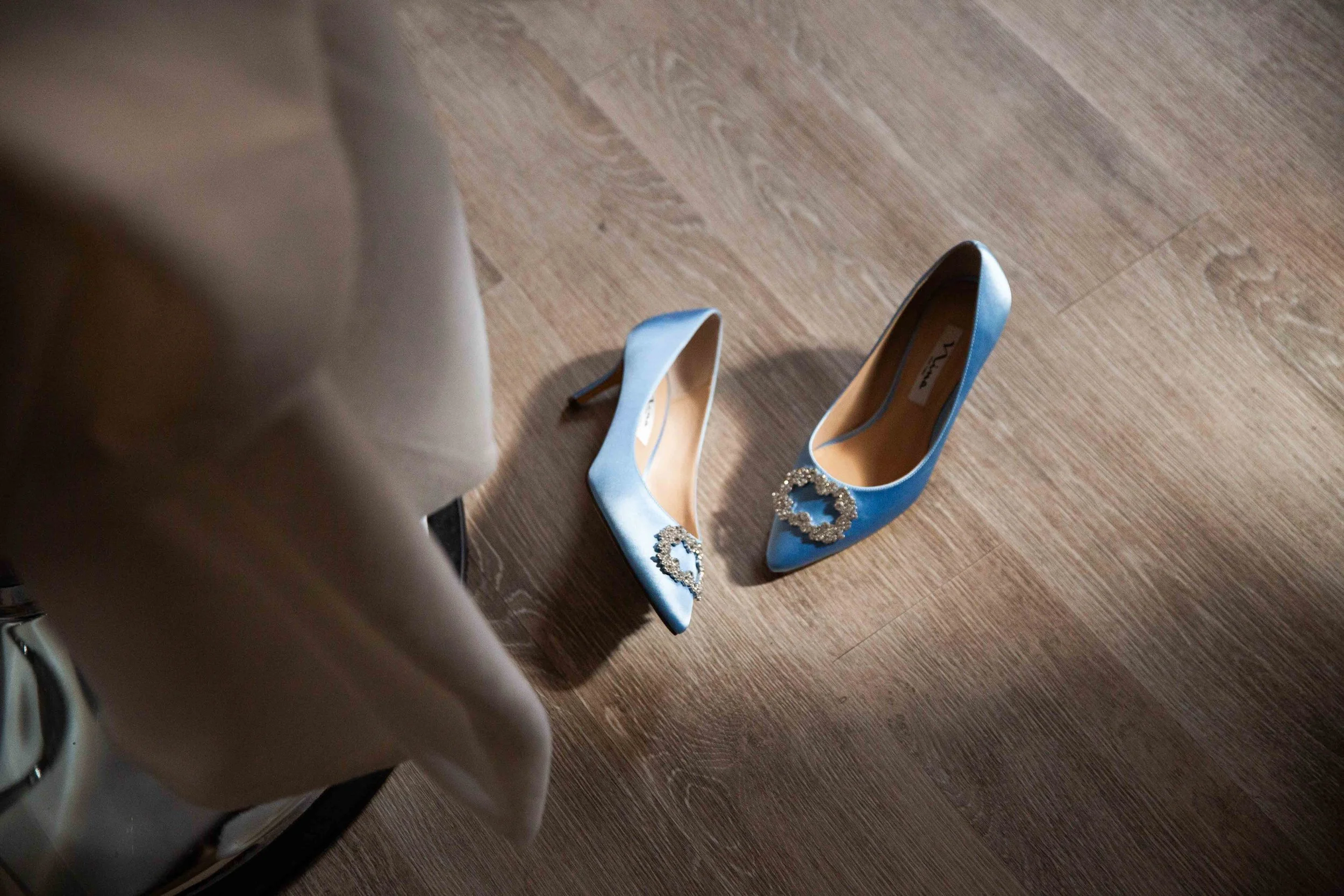 A pair of blue high-heeled shoes with decorative buckles on a wooden floor.