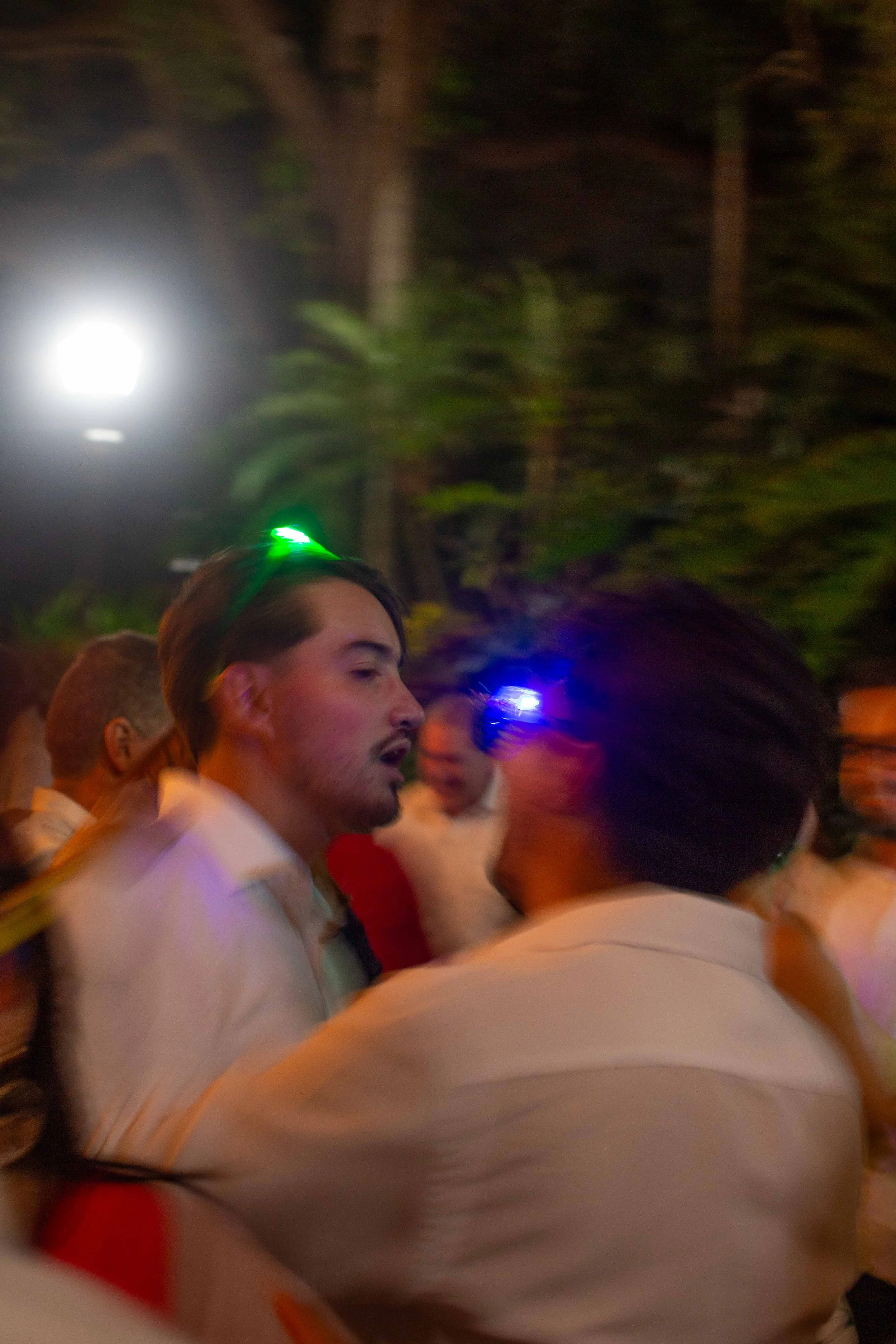 People dancing at a party or celebration at night, illuminated by colorful lights.