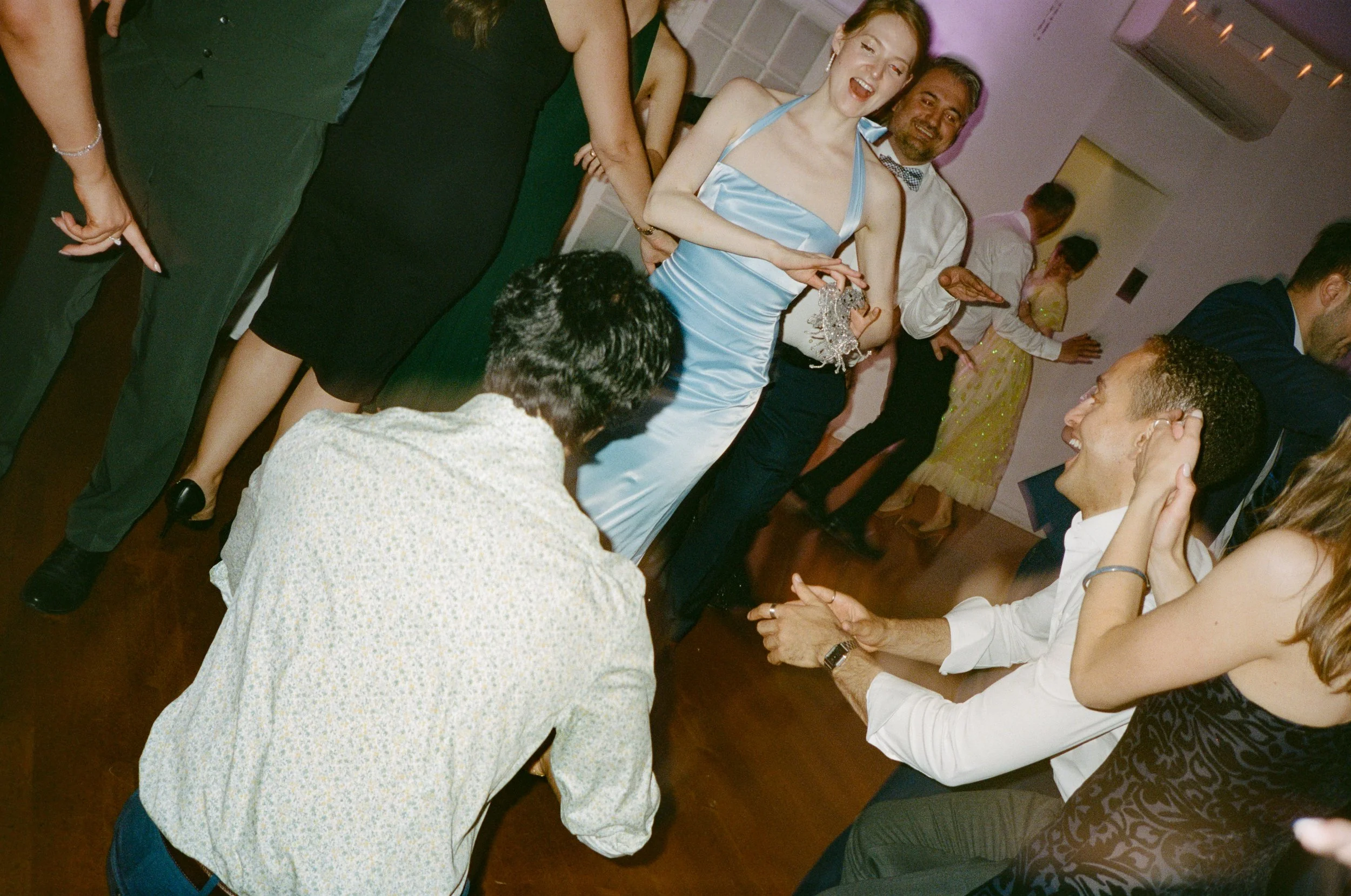 People dancing and socializing at a party or celebration, with some holding drinks and others talking or laughing.
