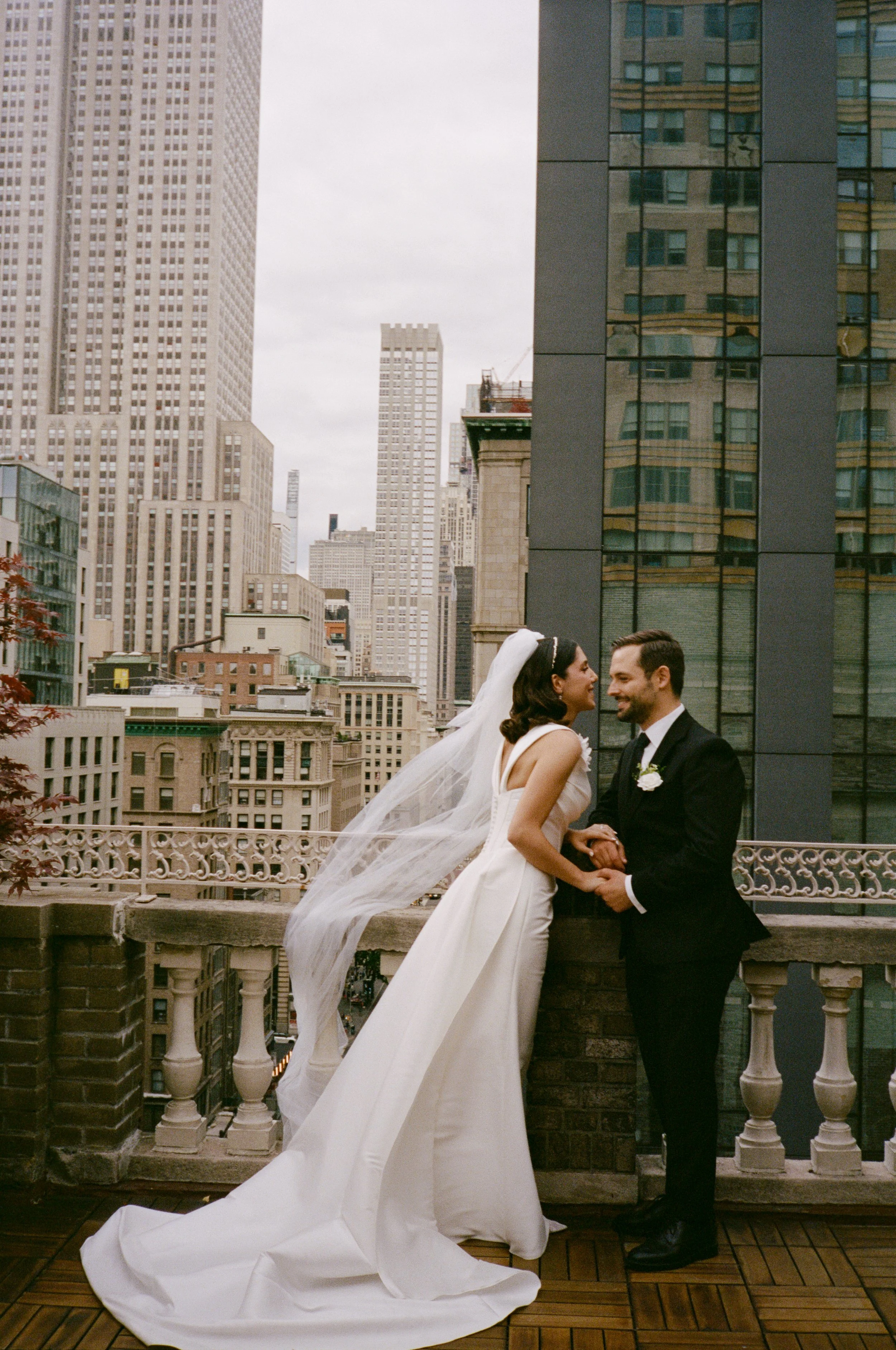 A bride and groom share a wedding moment on a rooftop with city skyscrapers in the background.