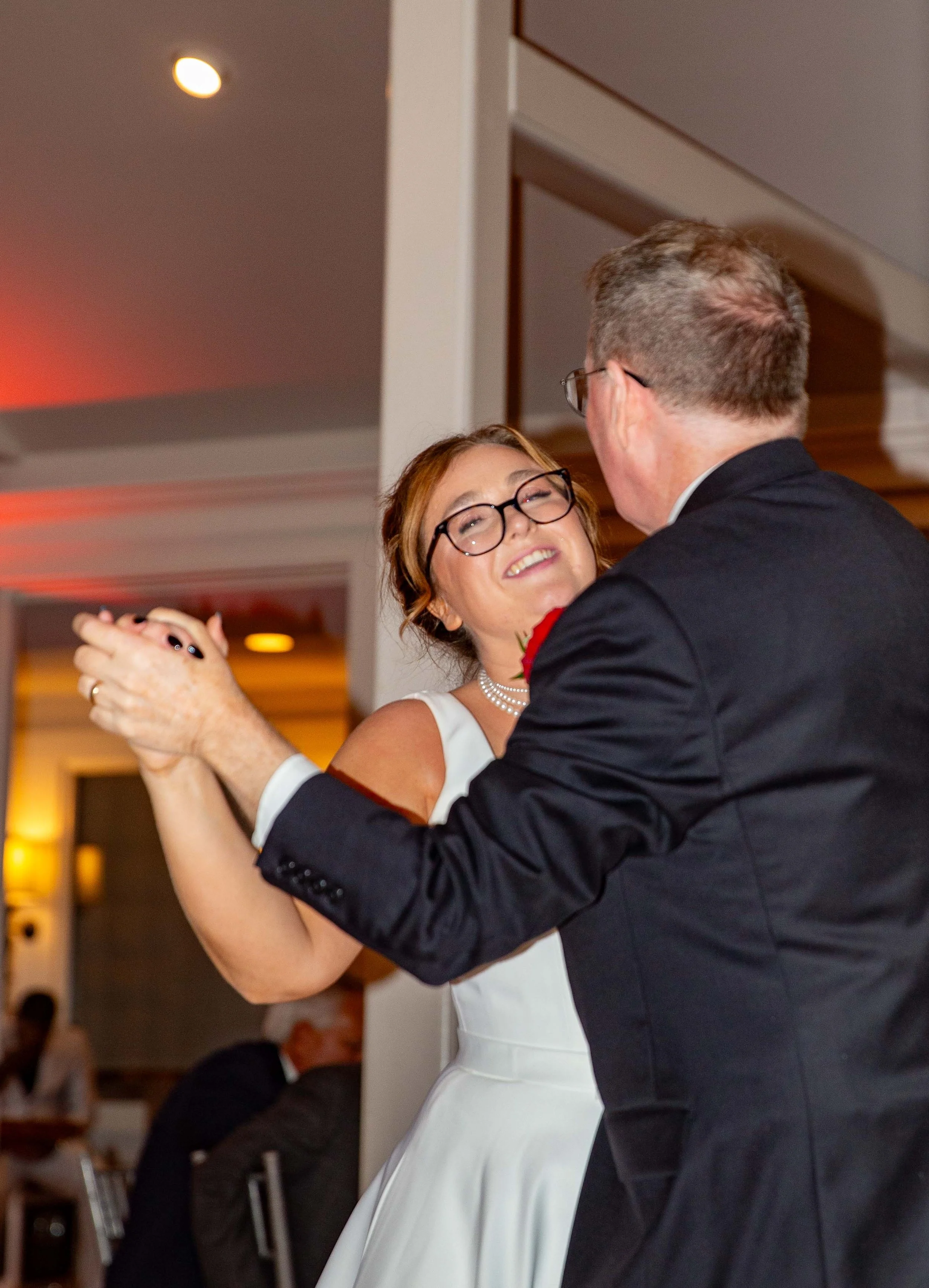 A woman and a man dancing together at a wedding reception, smiling and looking happy.